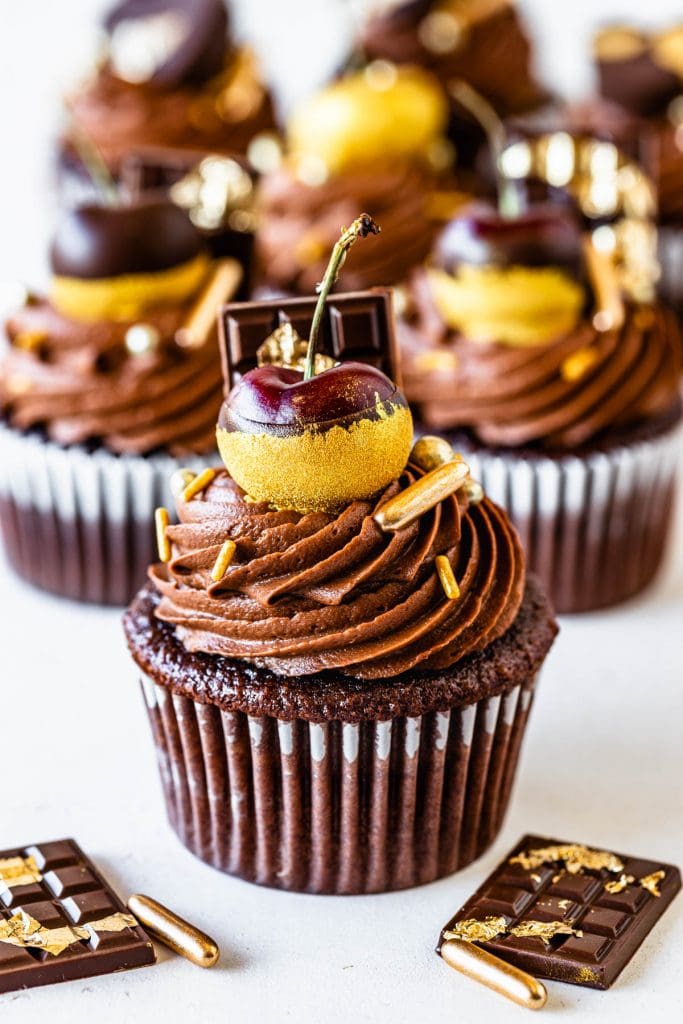 Chocolate Biscoff Cupcakes topped with a cherry dipped in gold dust, golden sprinkles.