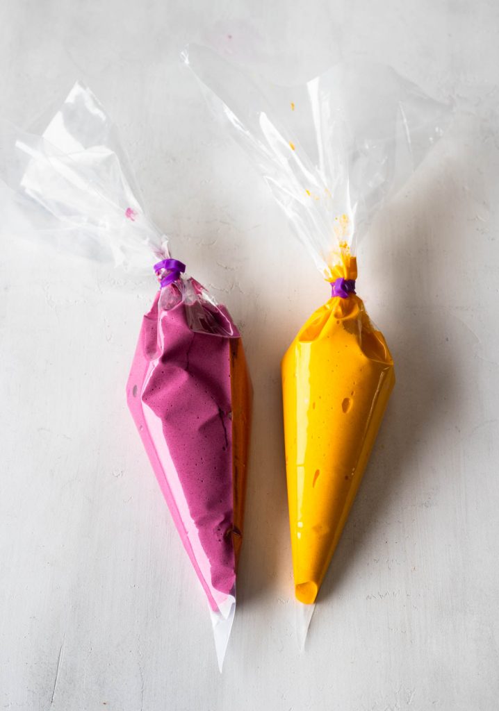 two piping bags filled with yellow and pink macaron batter.