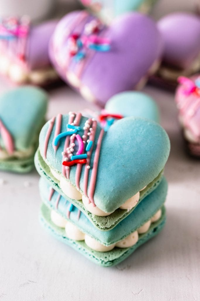 stacked heart macarons filled with brownies and cream cheese frosting, topped with a drizzle of melted chocolate and sprinkles.