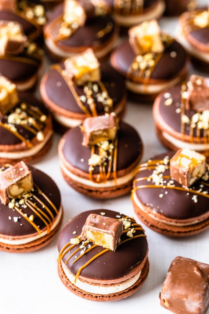 Snickers macarons filled with salted caramel, topped with caramel sauce and chopped snickers candy.
