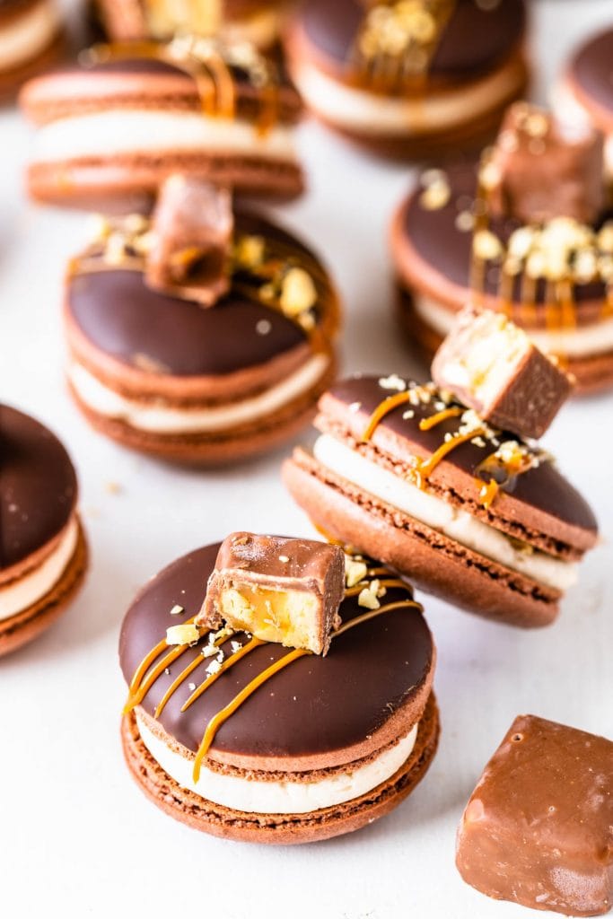 Snickers macarons filled with salted caramel, topped with caramel sauce and chopped snickers candy.