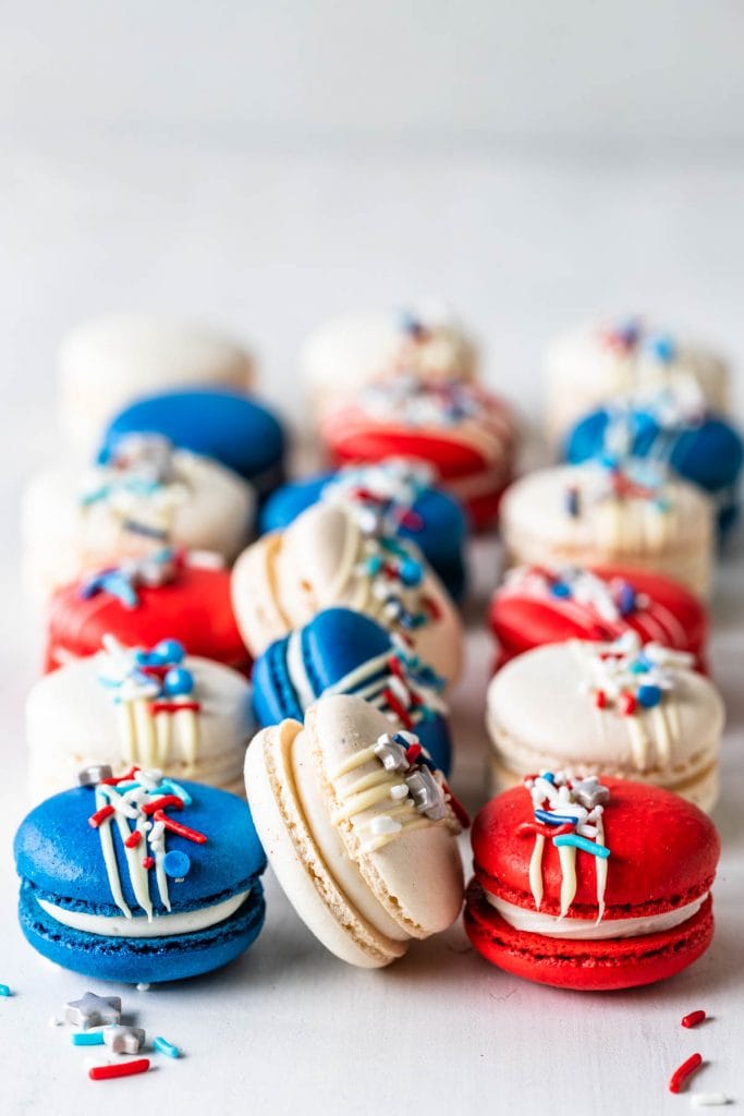 Red White and Blue Macarons topped with a white chocolate drizzle and sprinkles.