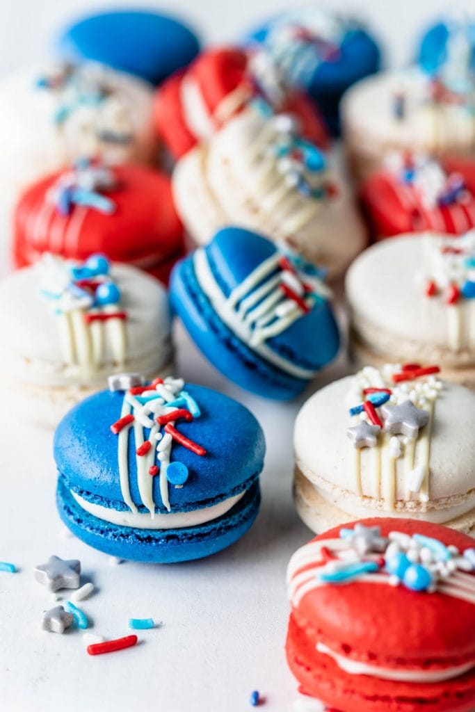 Red White and Blue Macarons topped with a white chocolate drizzle and sprinkles.