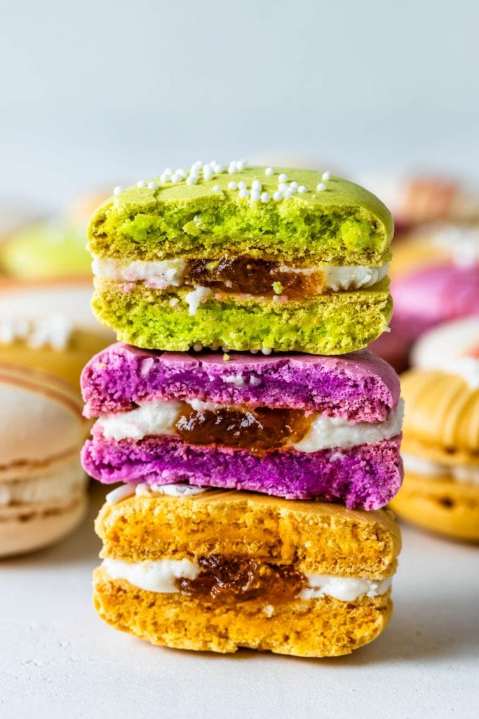 Colorful macarons, pink, red, yellow and white, with chocolate drizzle and sprinkles cut in half with apricot preserves filling.
