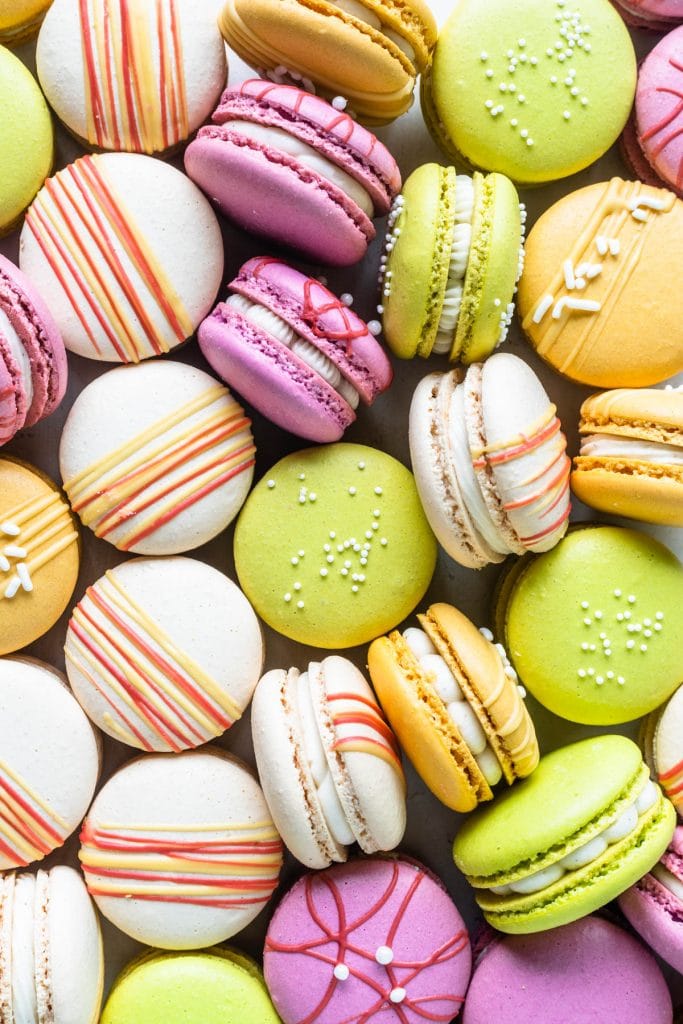 Colorful macarons, pink, red, yellow and white, with chocolate drizzle and sprinkles.