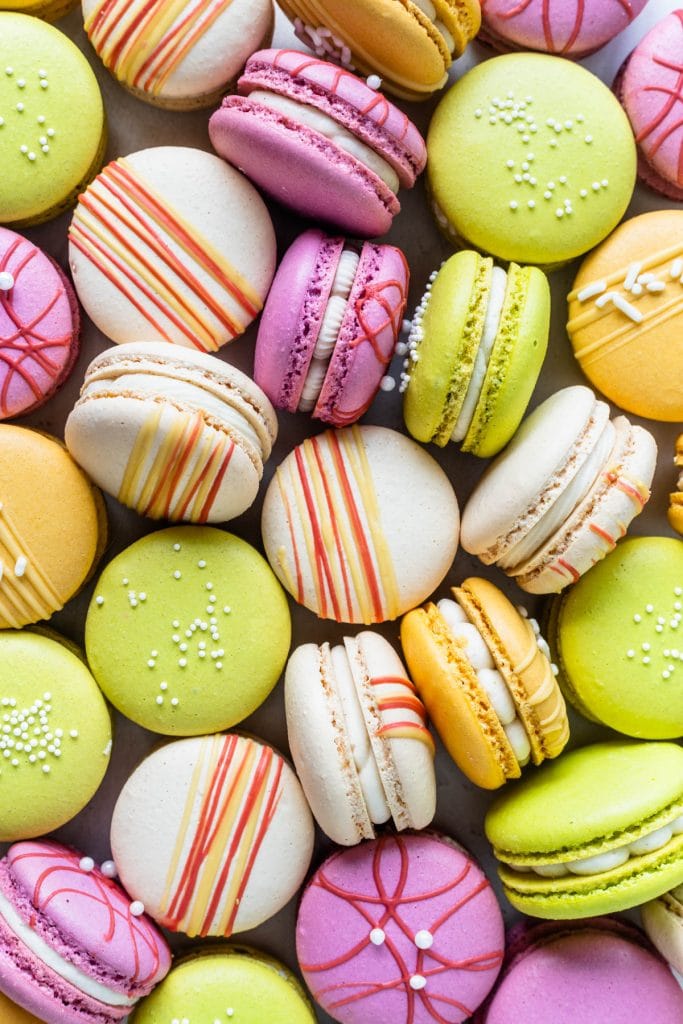 Colorful macarons, pink, red, yellow and white, with chocolate drizzle and sprinkles.