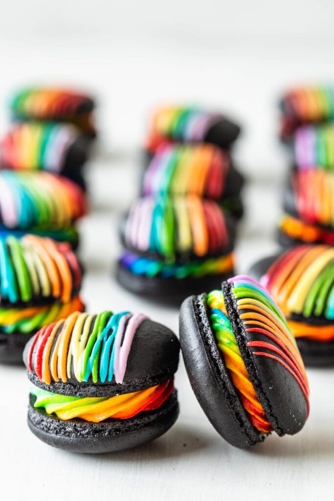 black and white macarons filled with rainbow frosting and topped with a rainbow colored drizzle.