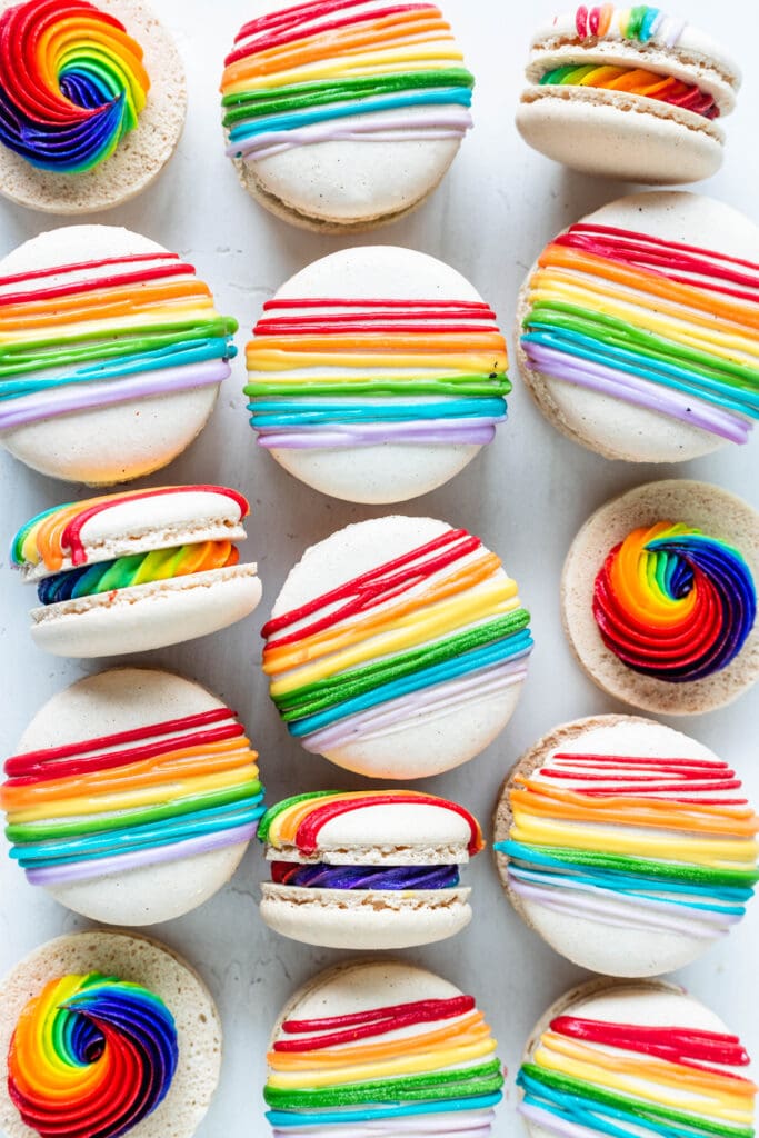 white macarons filled with rainbow frosting and topped with a rainbow colored drizzle.