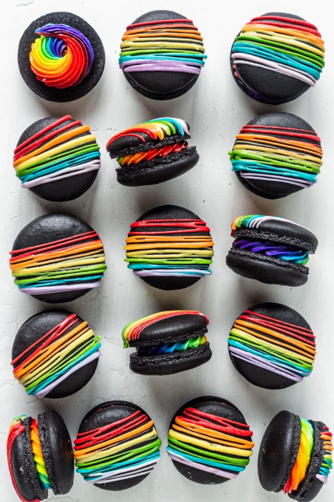 black macarons filled with rainbow frosting and topped with a rainbow colored drizzle.