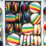 black and white macarons filled with rainbow frosting and topped with a rainbow colored drizzle.