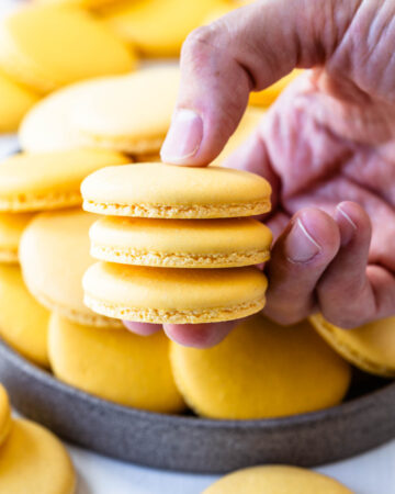 hand holding 3 macarons with more yellow macarons in the background.