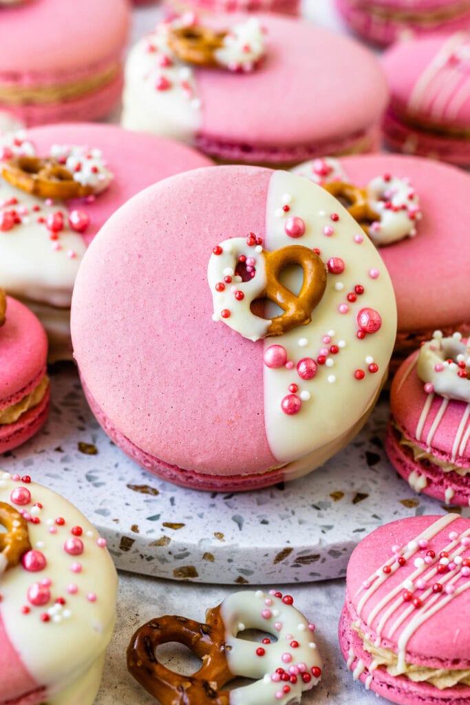 pink macarons dipped in white chocolate with a pretzel on top.