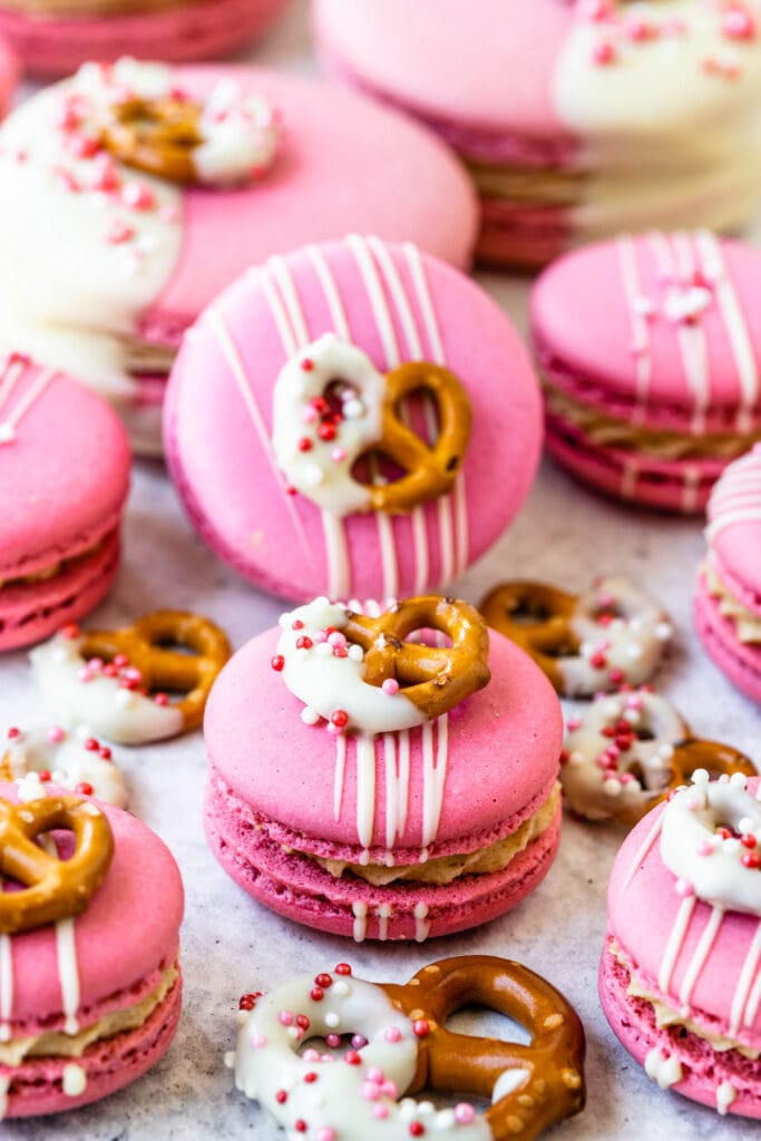 pink macarons dipped in white chocolate with a pretzel on top.