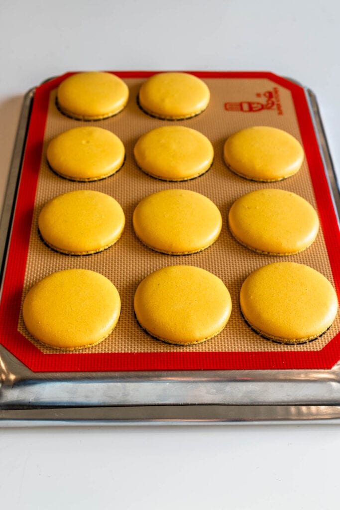 yellow macaron shells on top of a baking sheet made with no rest method.