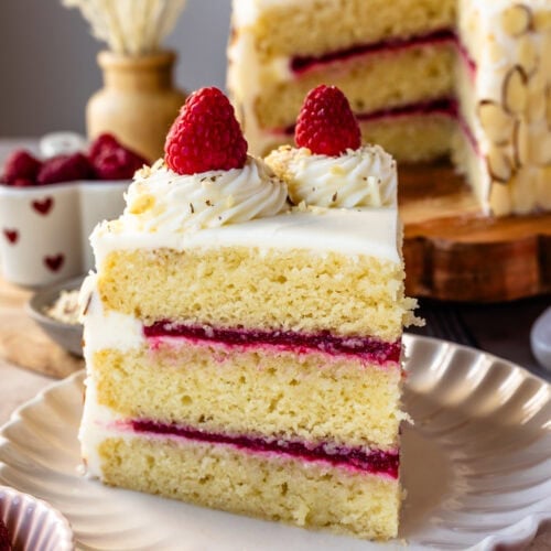 Slice of almond raspberry cake showing three layers of almond cake with raspberry filling and buttercream frosting.