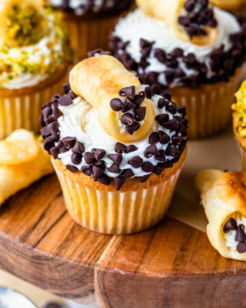 cupcakes topped with frosting and coated with mini chocolate chips, topped with a mini cannoli.