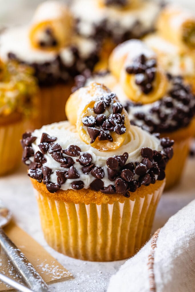 cupcakes topped with frosting and coated with mini chocolate chips, topped with a mini cannoli.