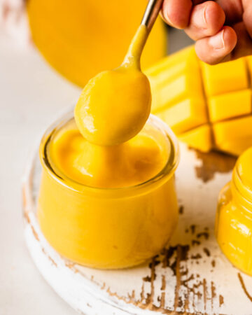 mango curd in a container with a spoon.