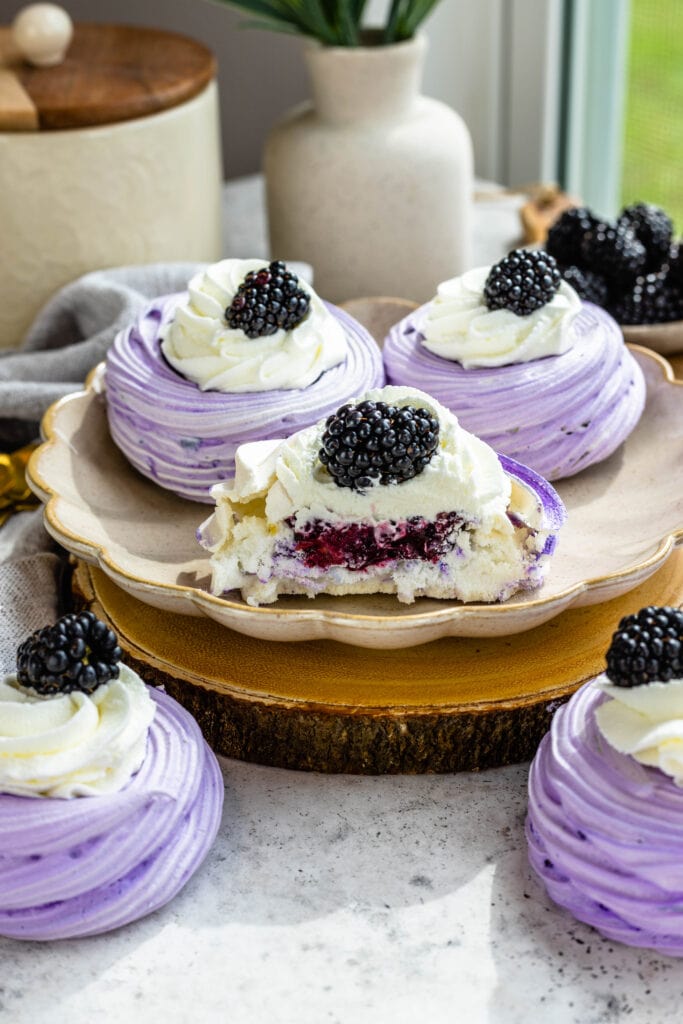 blackberry pavlovas, purple pavlovas topped with whipped cream and blackberries cut in half.