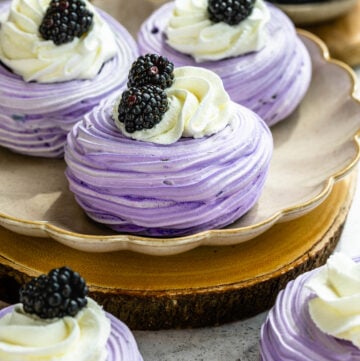 blackberry pavlovas, purple pavlovas topped with whipped cream and blackberries.