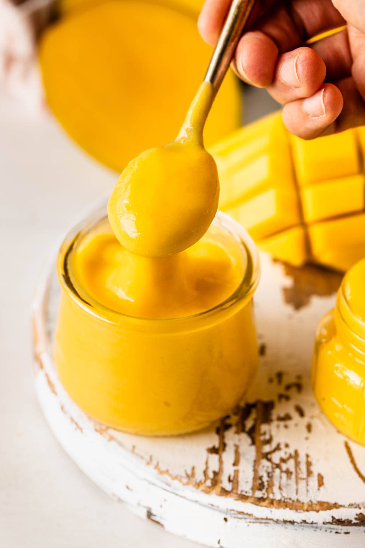 mango curd in a jar, with a spoon scooping some curd.