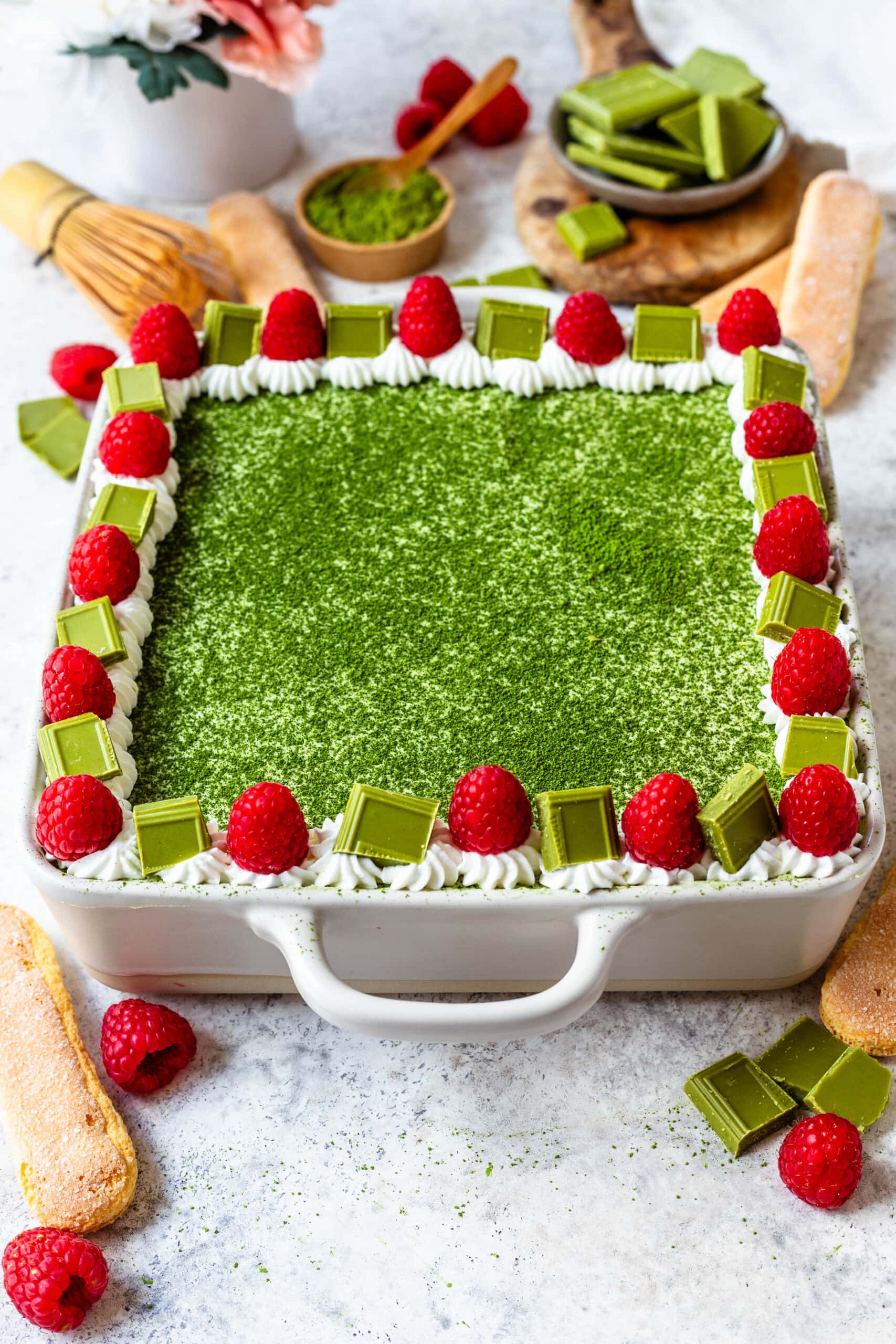 matcha tiramisu in a dish with raspberries and matcha chocolate on top.