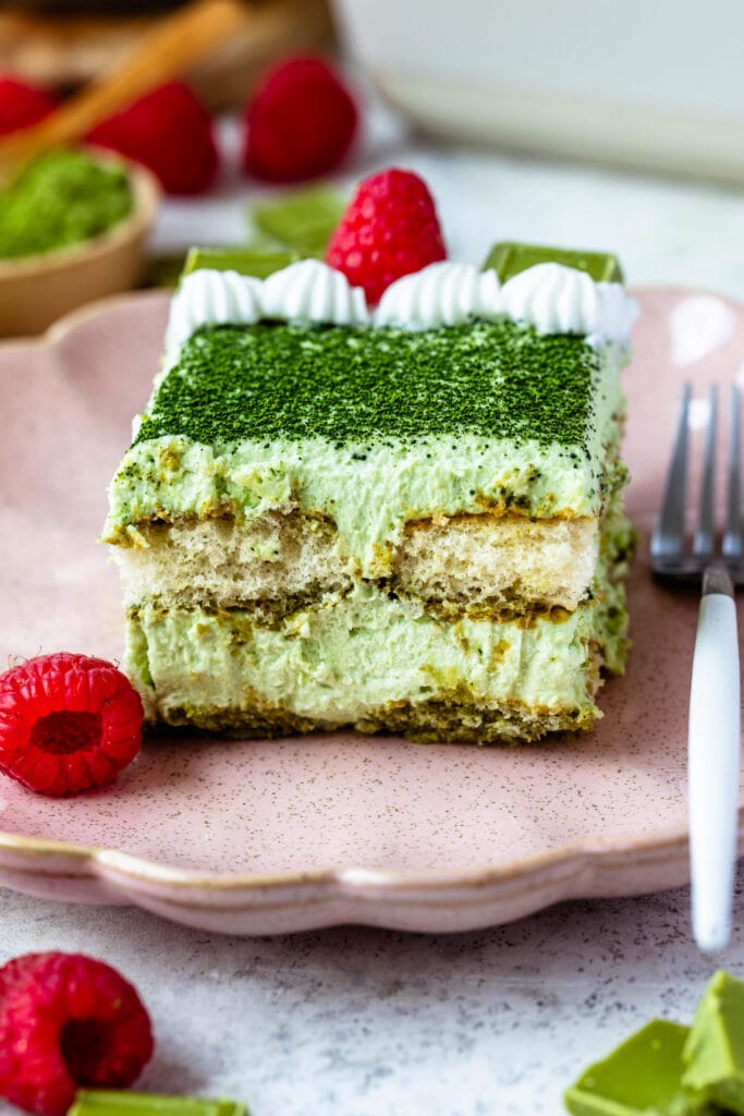 slice of Matcha Tiramisu on a pink plate with raspberries on top and on the side.