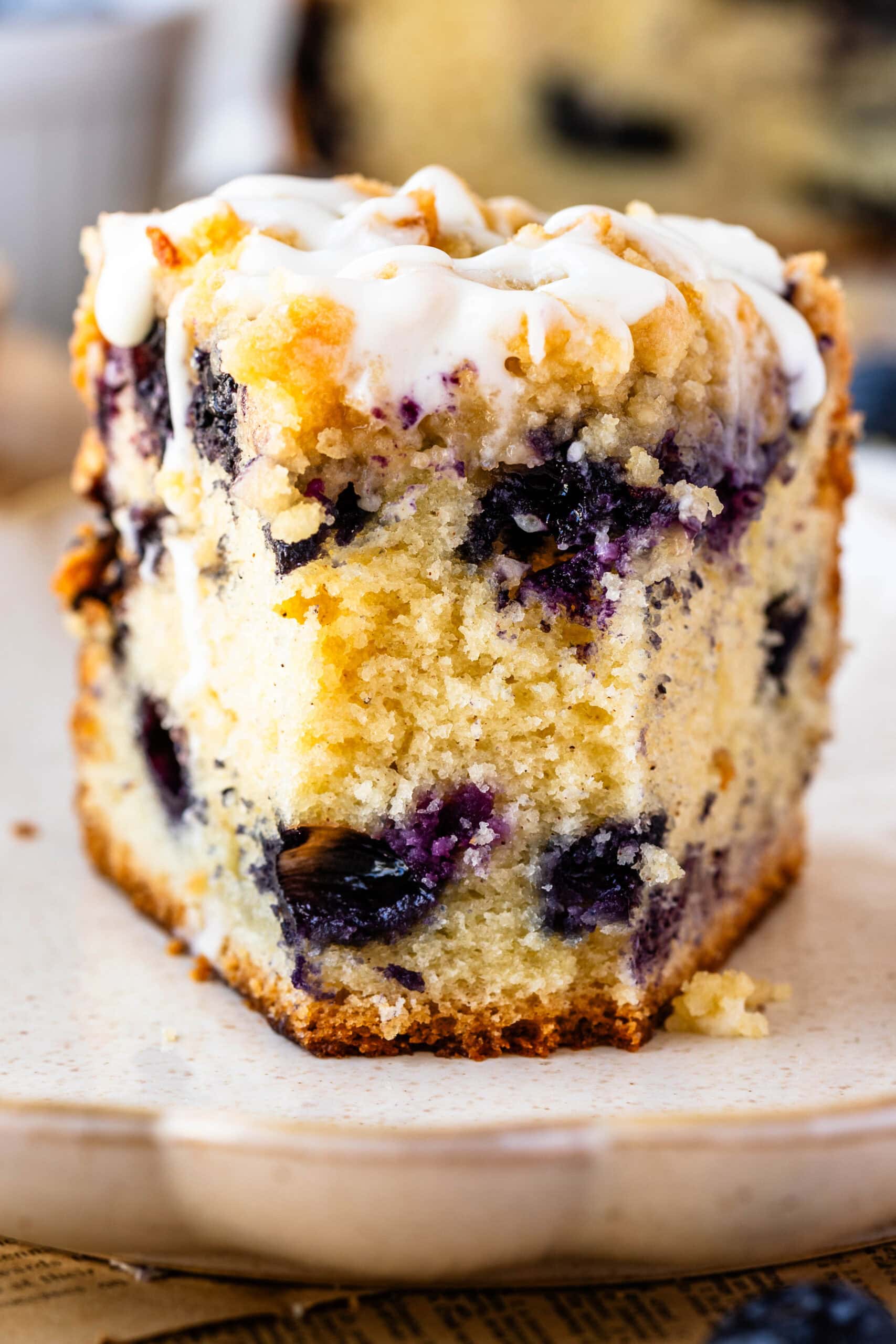 Close-up of a slice of blueberry crumb cake filled with fresh blueberries, topped with buttery streusel and a drizzle of vanilla glaze.