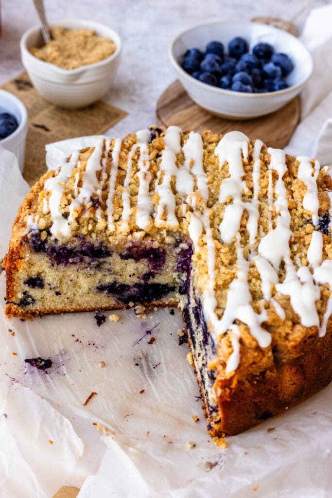 blueberry coffee cake sliced, showing the center filled with blueberries, and the crumble topping with glaze spread all over.