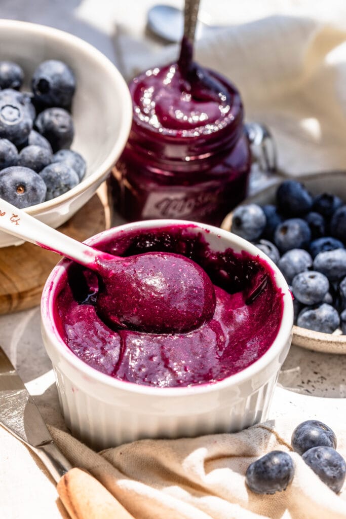 blueberry curd in a bowl with a spoon, and blueberries close by.