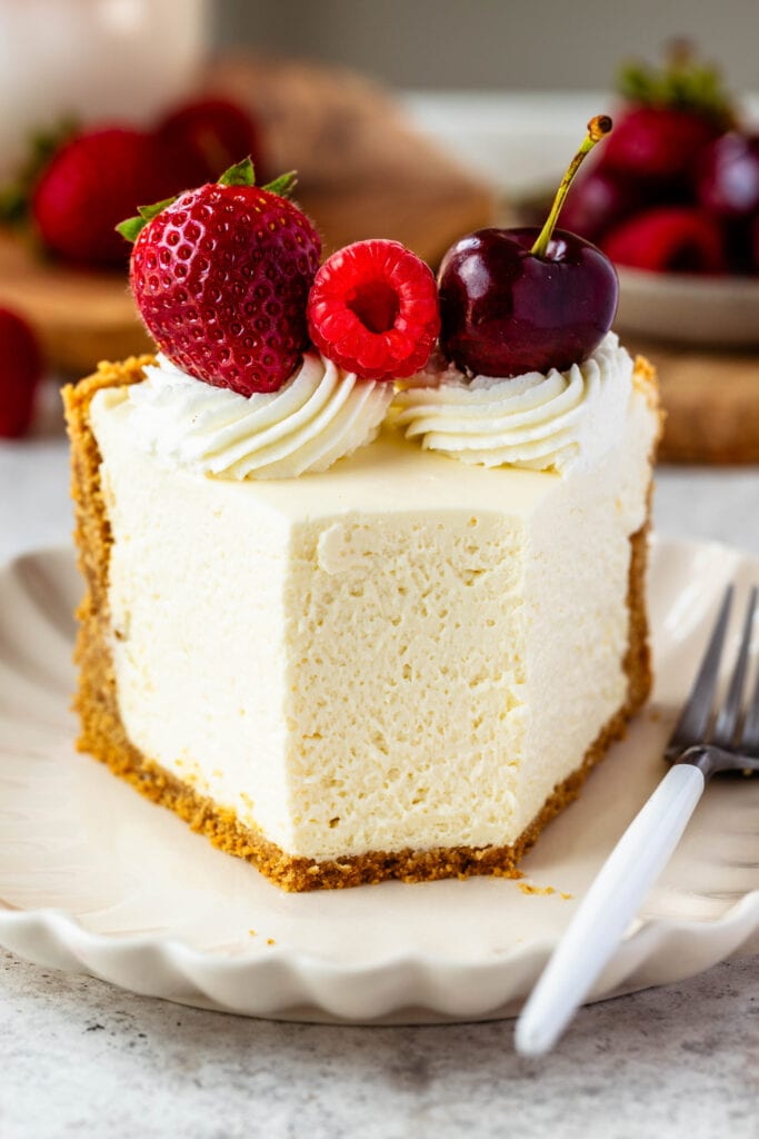 slice of cheesecake with cherries, strawberries, and raspberry on top.