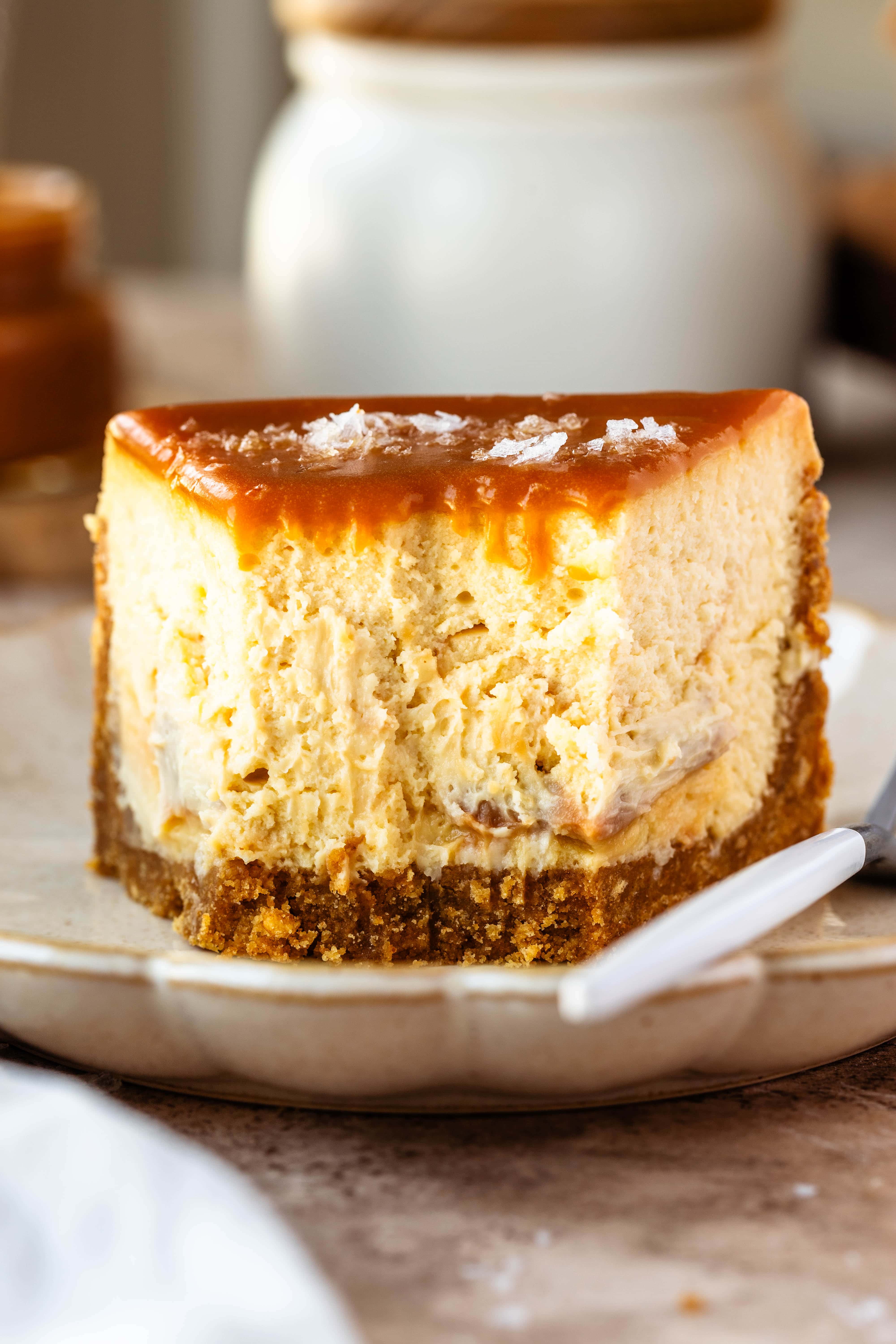 Slice of cheesecake on a plate topped with caramel sauce, with caramel on top and salt flakes.