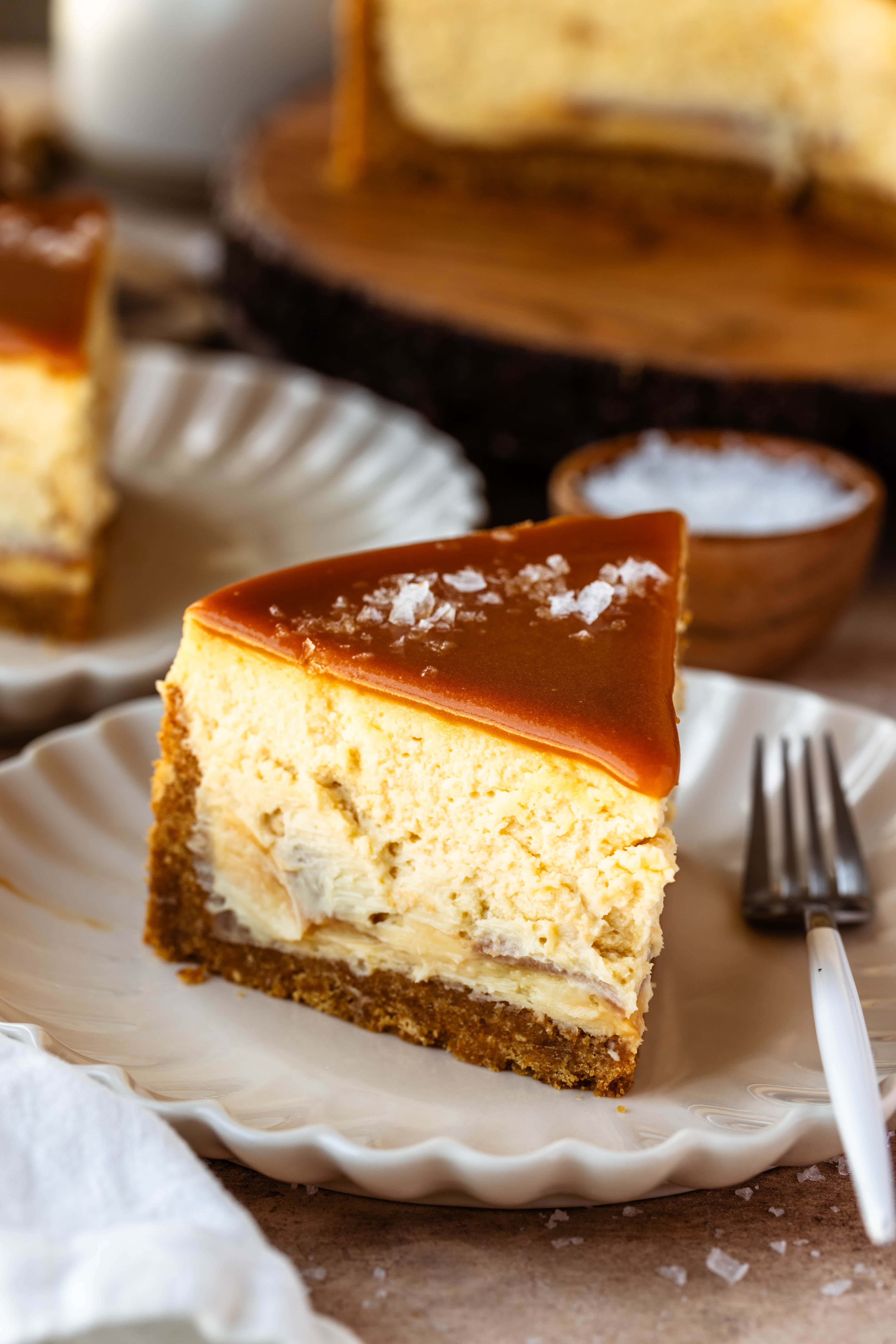 Slice of caramel cheesecake on a plate, with caramel on top and salt flakes.