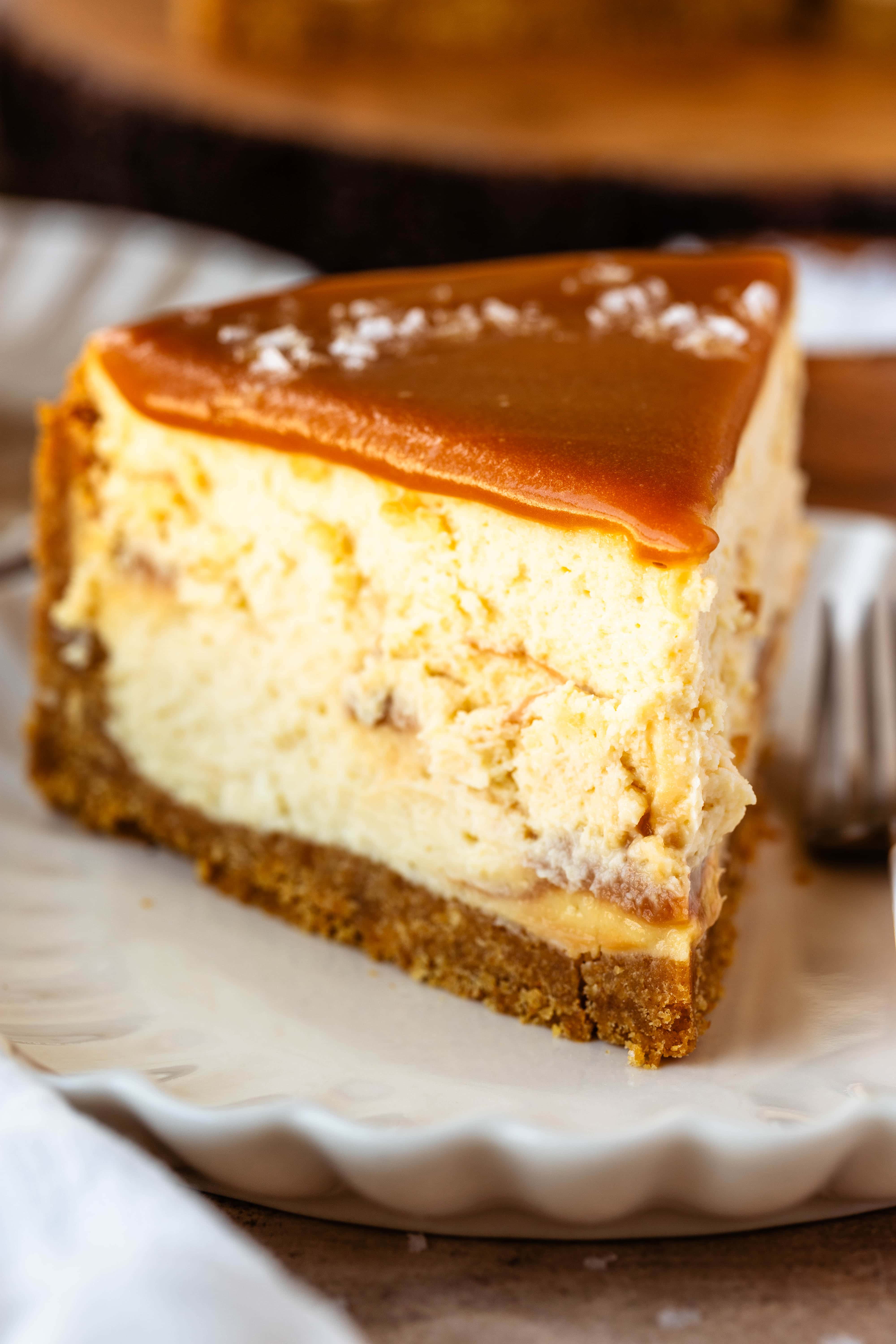 Slice of caramel cheesecake on a plate, with caramel on top and salt flakes.