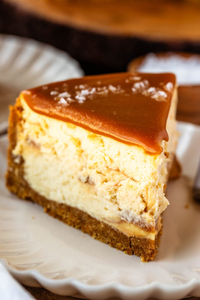 Slice of caramel cheesecake on a plate, with caramel on top and salt flakes.