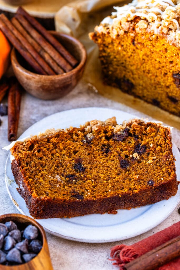 slice of pumpkin bread on a plate, with cinnamon sticks in the back.