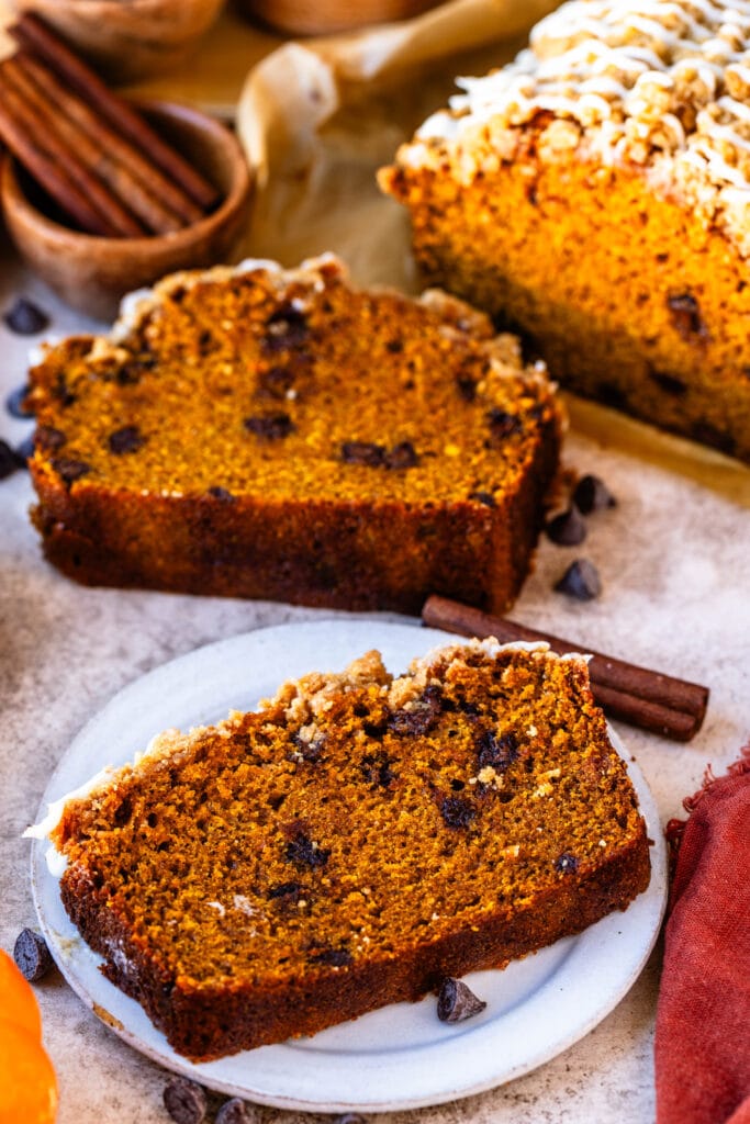 pumpkin bread recipe sliced with chocolate chips in the batter, with pumpkins around.