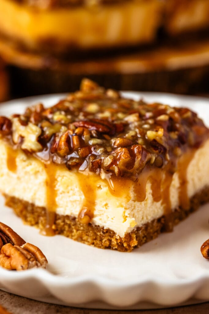 slice of pecan pie cheesecake bar with caramel pecan on top.