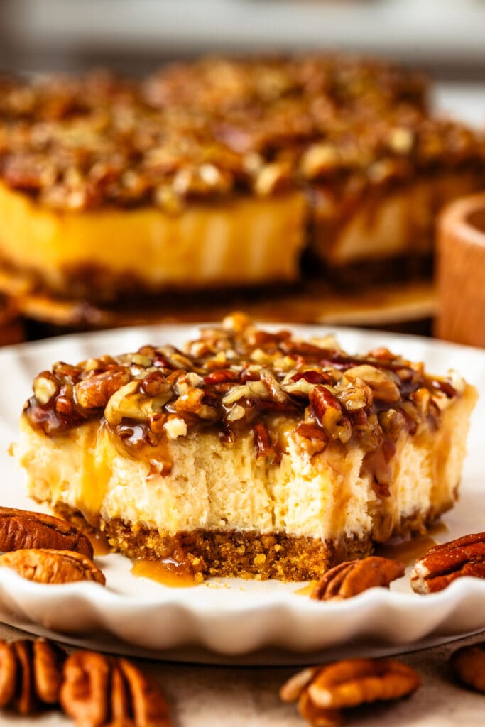 slice of pecan pie cheesecake bar with caramel pecan on top.