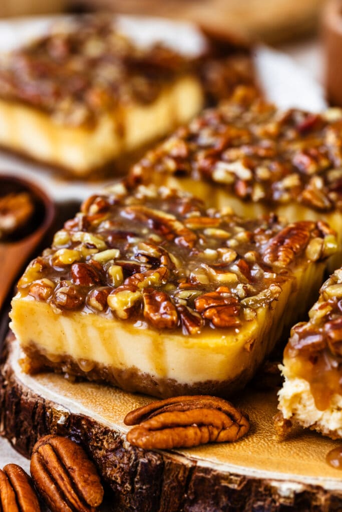 slice of pecan pie cheesecake bar with caramel pecan on top.