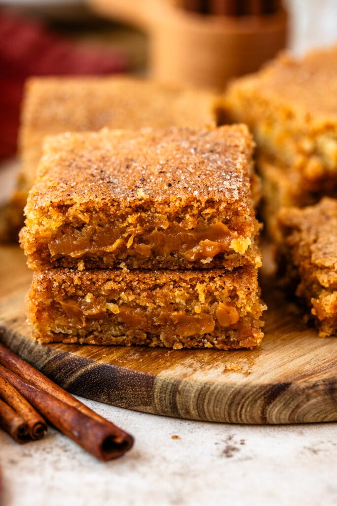 snickerdoodle filled dulce de leche bars stacked on top of the other, with cinnamon sticks on the side.