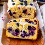 blueberry lemon bread with lemon glaze on top, sliced on top of a wooden plate.