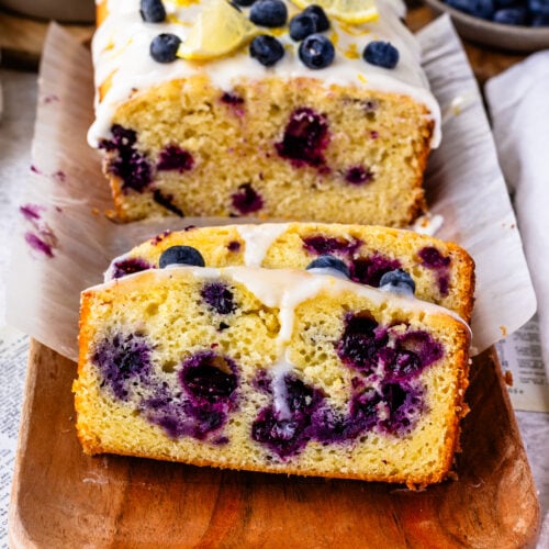 blueberry lemon bread with lemon glaze on top, sliced on top of a wooden plate.