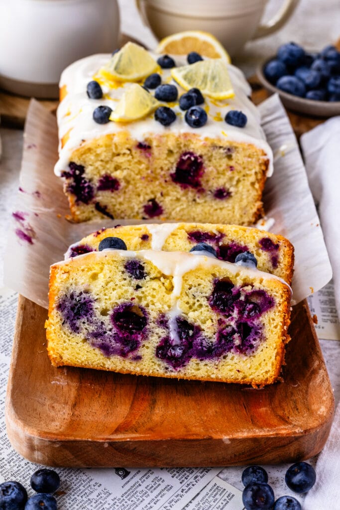 blueberry lemon bread with lemon glaze on top, sliced on top of a wooden plate.