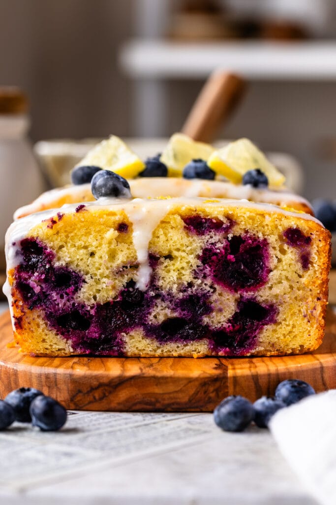 blueberry lemon bread with lemon glaze on top, sliced on top of a wooden plate.