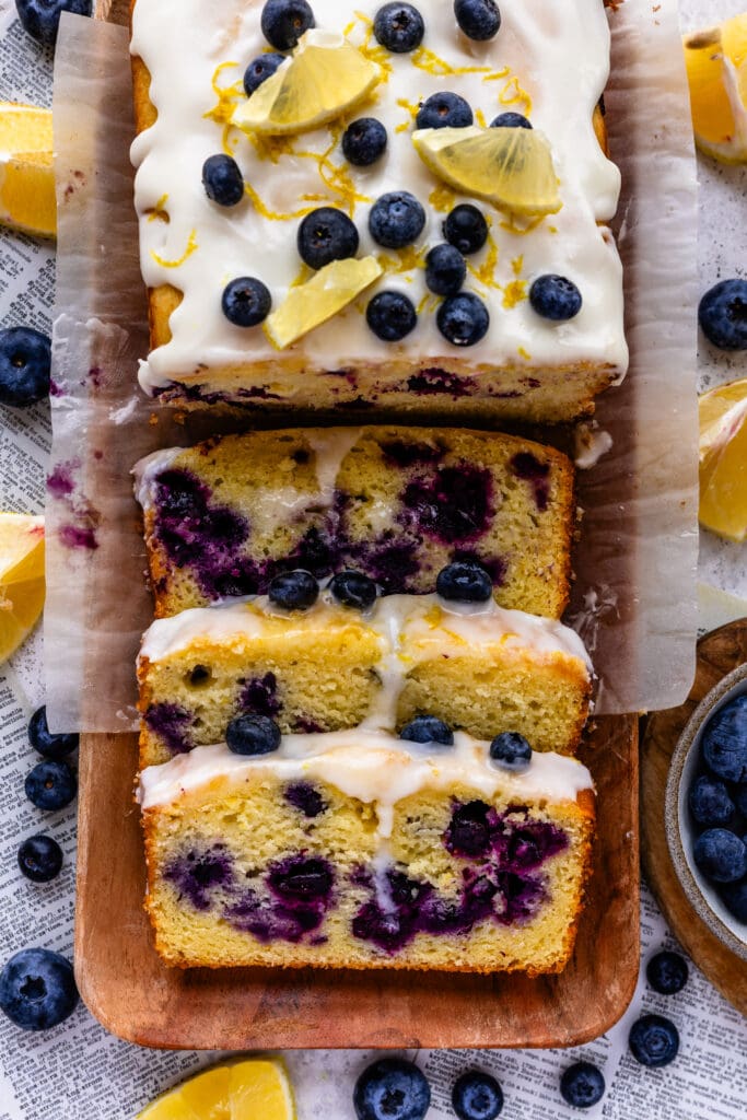 blueberry lemon bread with lemon glaze on top, sliced on top of a wooden plate.
