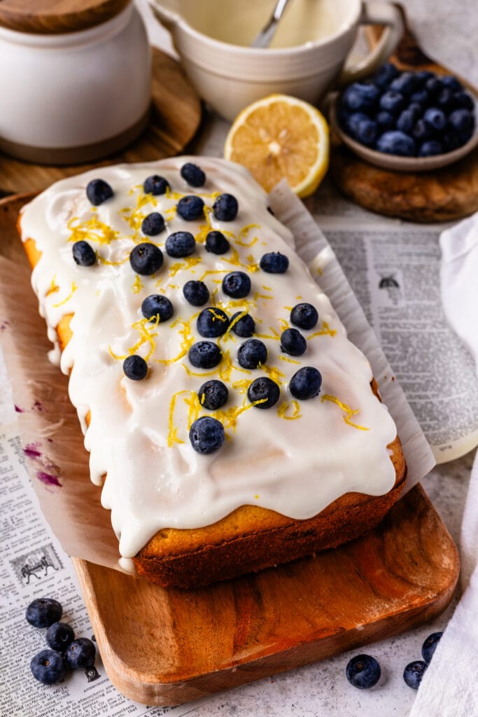 blueberry lemon bread with lemon glaze on top, on a wooden plate.