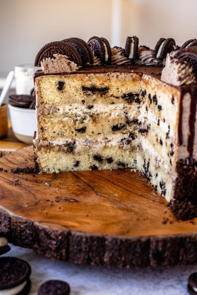 sliced cookies and cream cake on a wooden board, with a cookies and cream mousse filling, topped with a ganache drip.