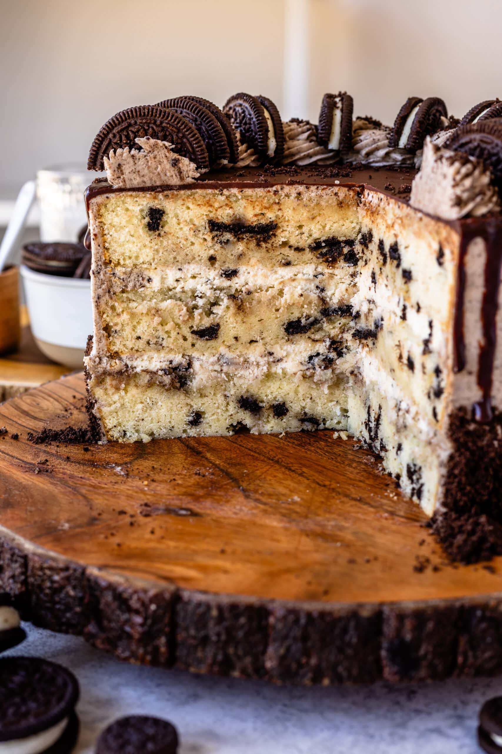 sliced cookies and cream cake on a wooden board, with a cookies and cream mousse filling, topped with a ganache drip.