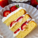 slice of strawberry shortcake cake on a plate, with whipped cream and fresh strawberries in the middle.